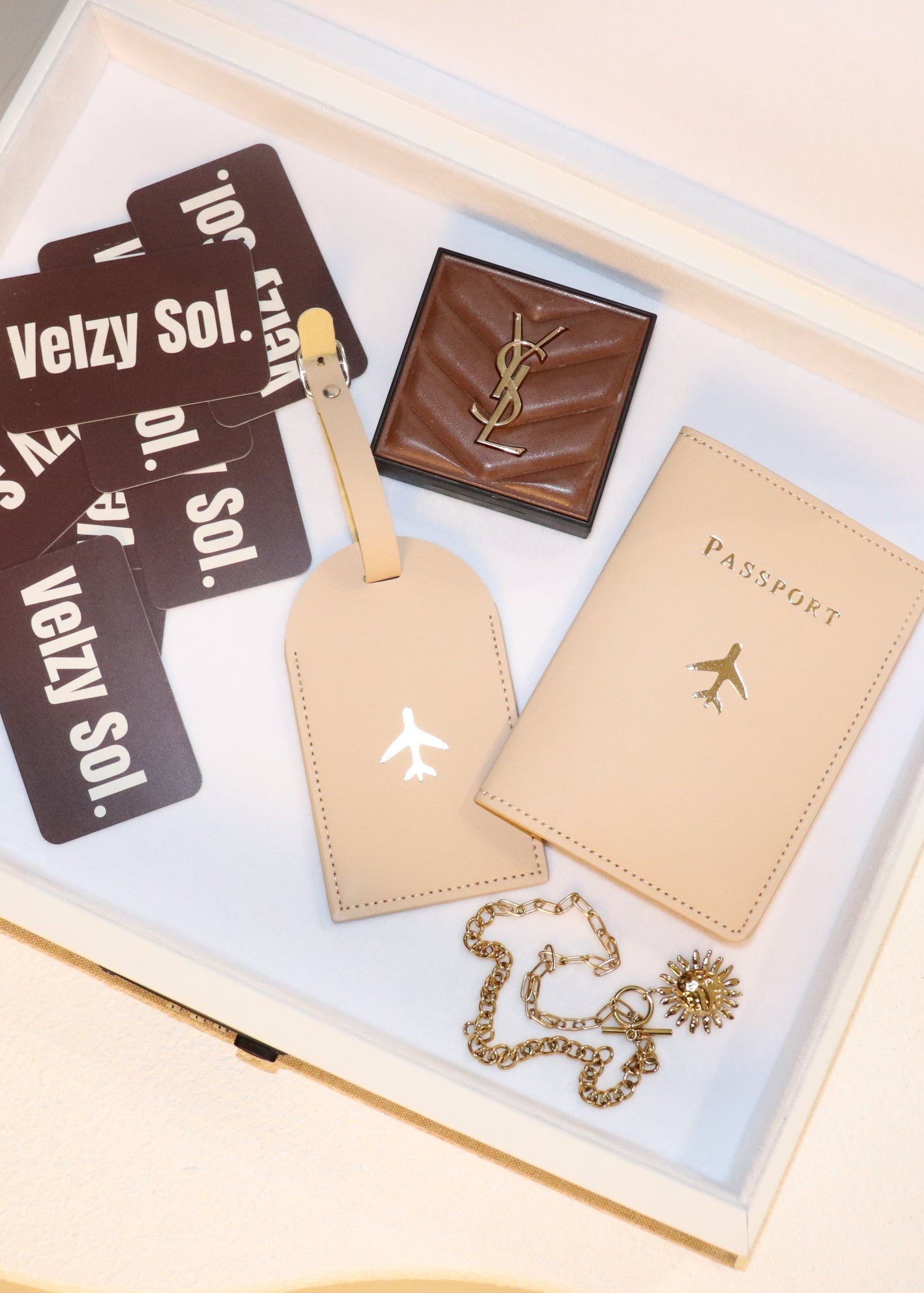 Collection of travel-related items including cards, a passport holder, and a compact mirror imside a velzy sol book box white velvet interior.